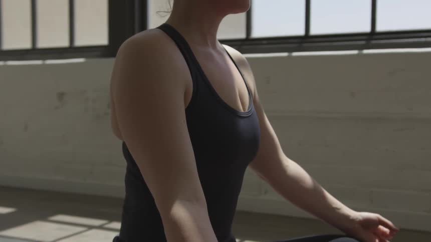 A woman is sitting on a yoga mat with her legs crossed palms out and eyes closed