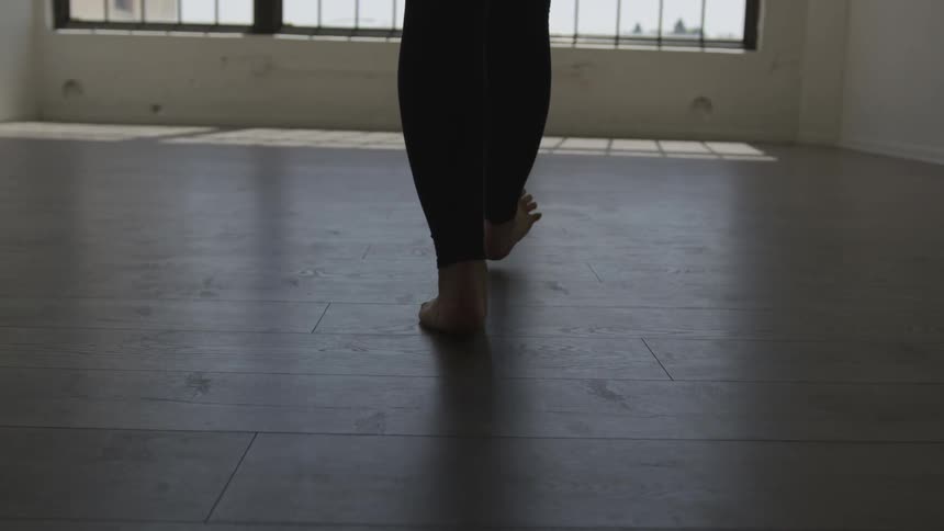 A woman in tights walks toward a set of windows in a dance studio