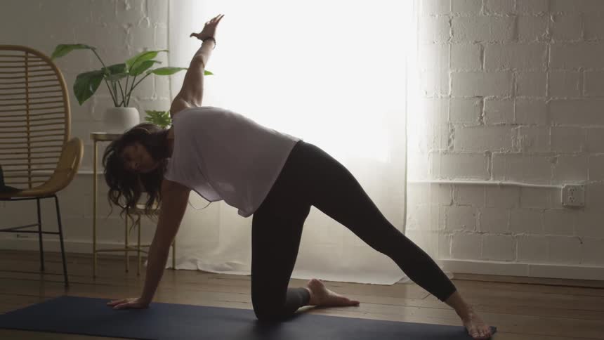 A woman does yoga indoors on a yoga mat
