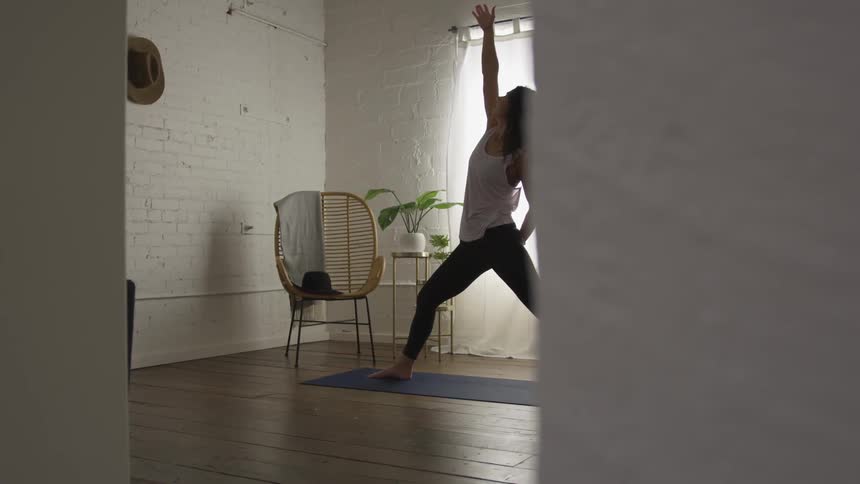 A woman is doing a full body stretch while standing on a yoga mat in a room