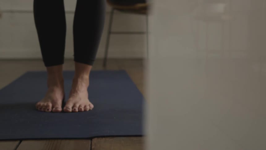 A woman is standing and stretching down and forward on a yoga mat
