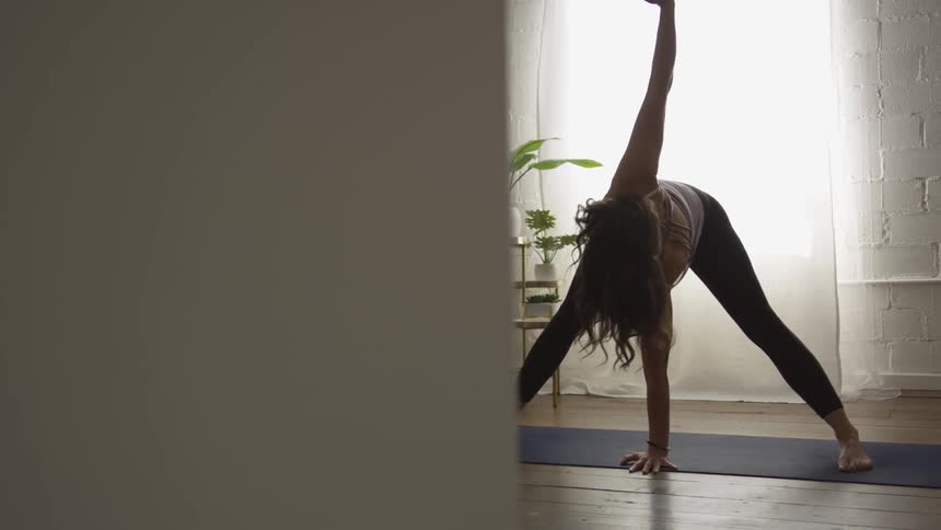 A young woman performing yoga in a white walled room