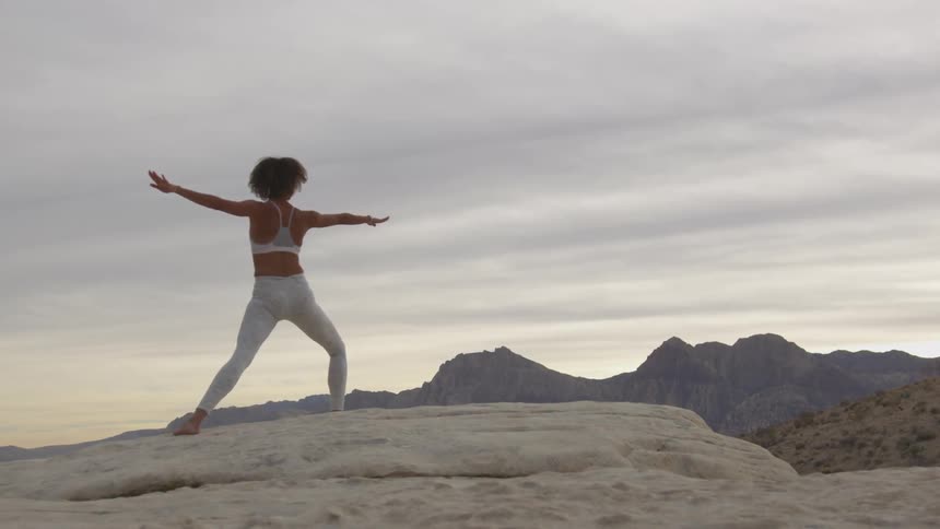 A woman stands on a rocky hill and does a full body stretch