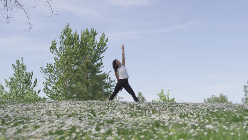 A woman does a yoga pose on top of a hill on a summer day