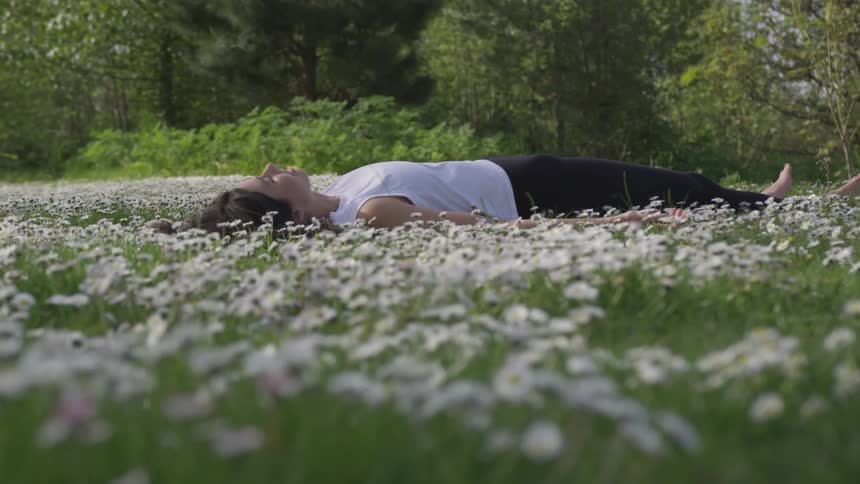 A white woman lies on her back in a field of daisies