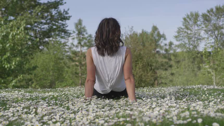A woman sits on a hill covered with daisies