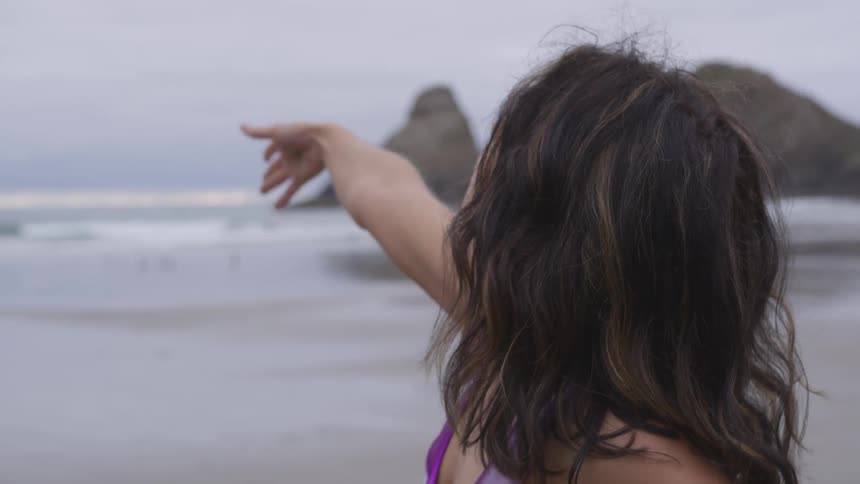 A woman is standing on the beach and stretching her arm to the sky