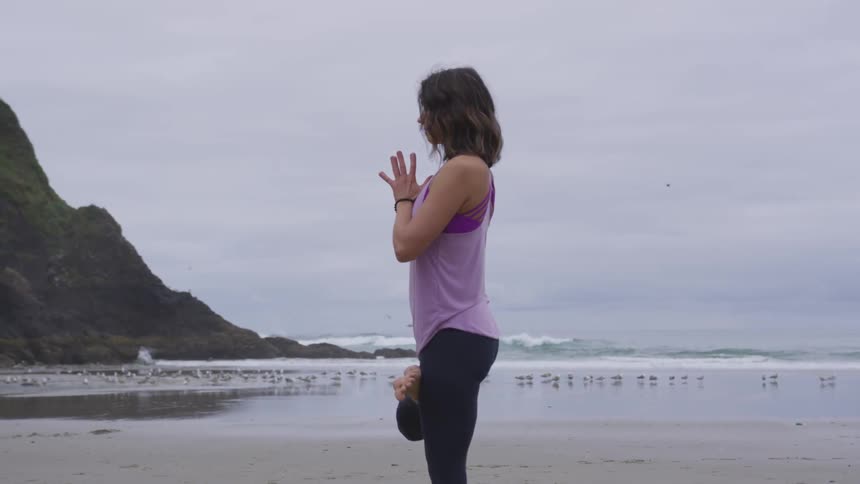 Woman practicing yoga on the shoreline of a beach