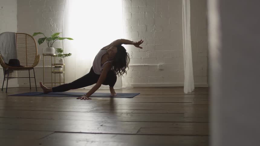 A woman crouches and leans to the side while stretching and doing yoga