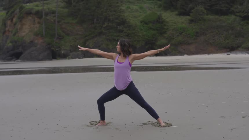 A woman in yoga pants does yoga on a sandy beach