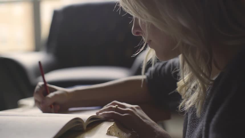 A white woman writes with a pencil in a book