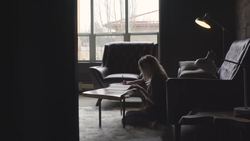A woman is sitting on the floor and writing in a workbook on a coffee table