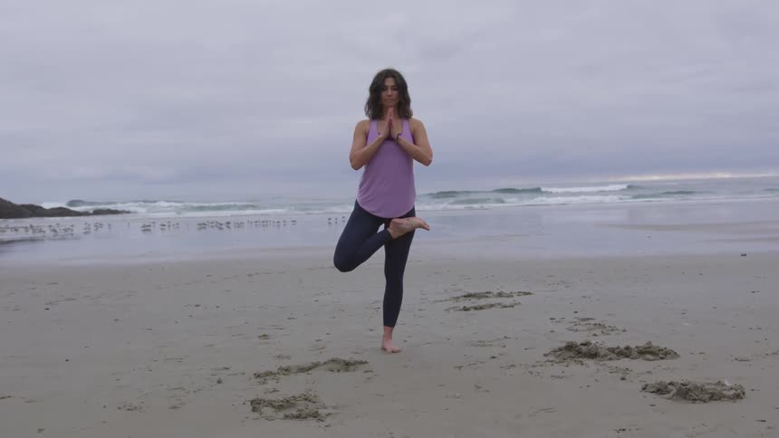 A woman on the beach meditating on one leg
