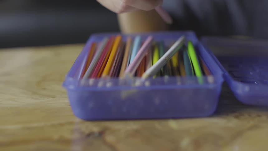 Hand picks up a colored pencil from a box