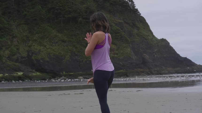 A woman stands on the beach in a yoga pose