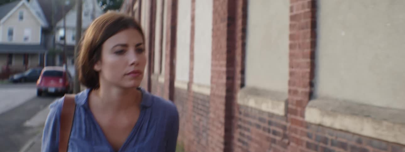 A woman walks down the sidewalk by a brick building