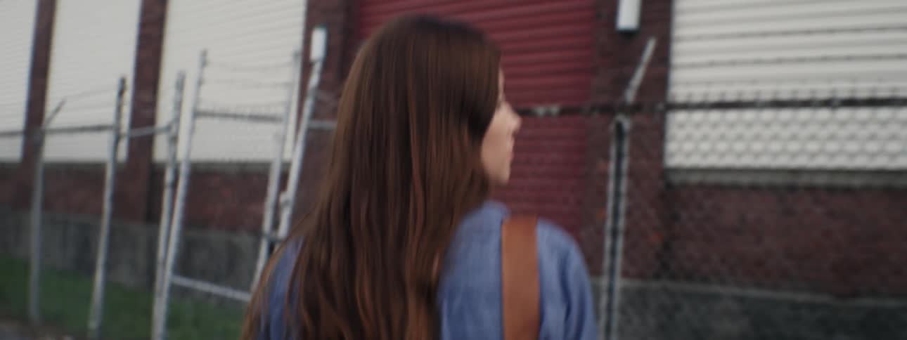 Woman looks over her shoulder as she walks alongside a fence