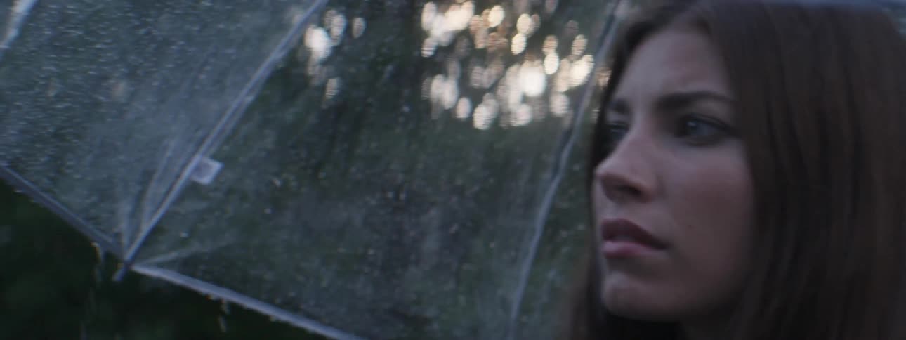 A young woman walking as rain falls on her clear umbrella