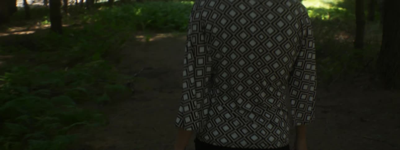 A woman is walking through the woods where the sunlight barely shines through
