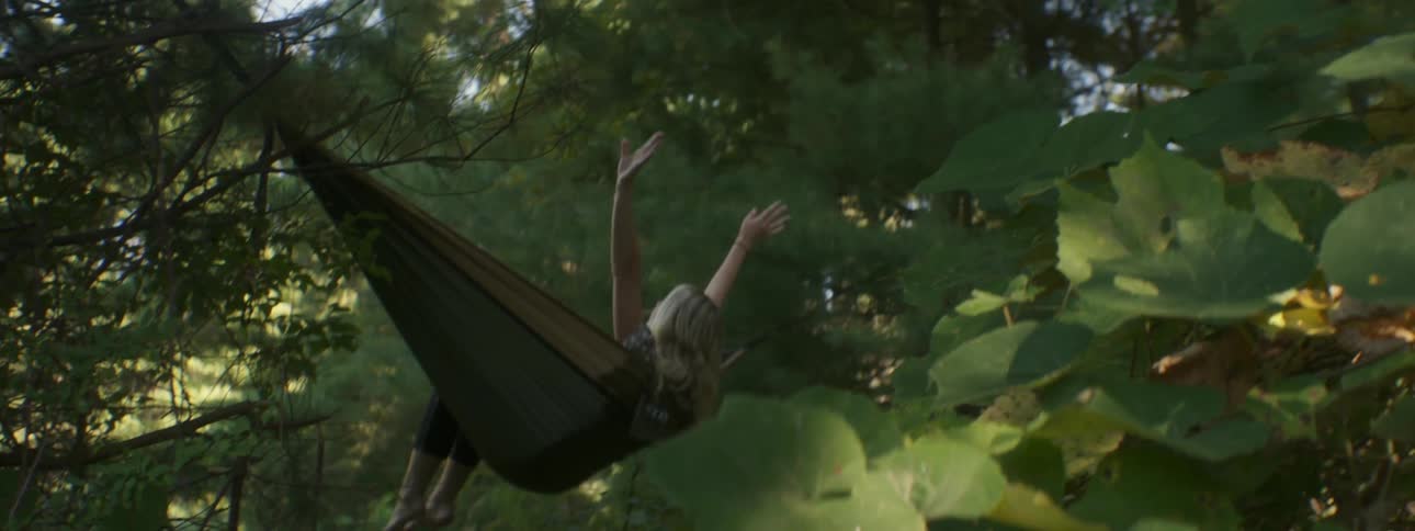 A woman swings back and forth on a hammock in the forest