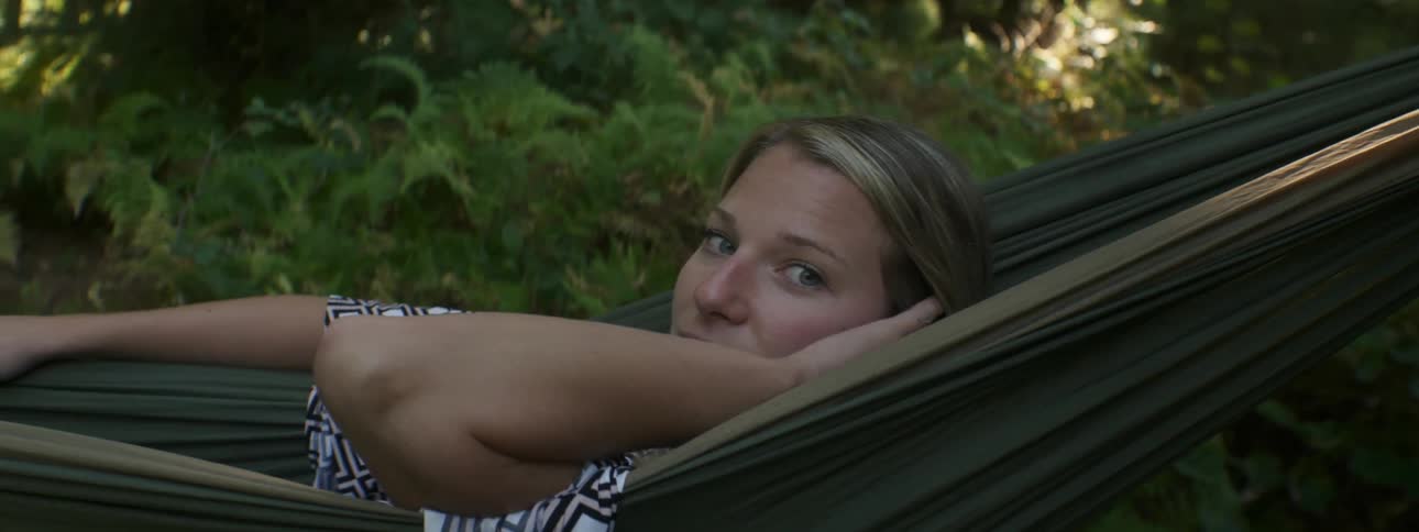 A woman swings in a hammock and brushes her hair