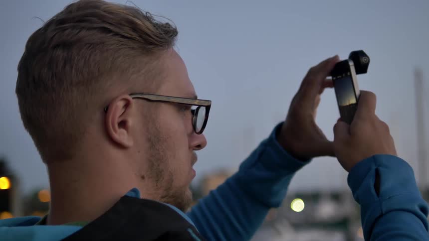 A young, blonde man taking a picture with his phone