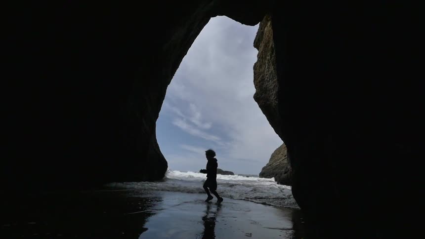 Child dances in the water underneath a cliff