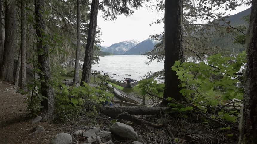 View of a woman swinging in a hammock with a body of water and mountains in the background