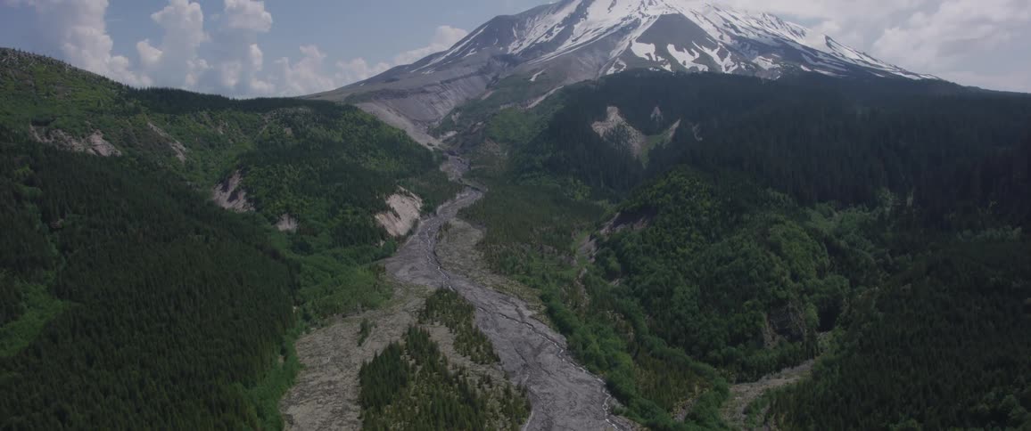 High above a range of already very tall mountains an enormous mountain capped with snow stands with its summit in the clouds