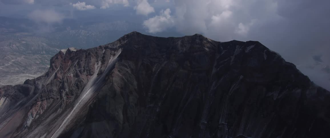 Clouds cover part of a tall mountain peak with snow on the bottom