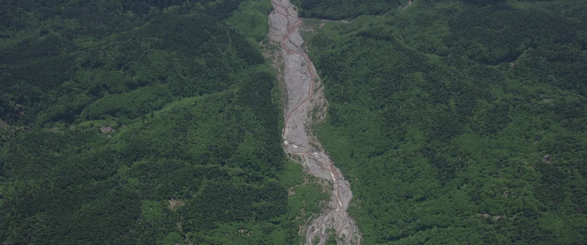 The camera looks down on a river winding through a forest