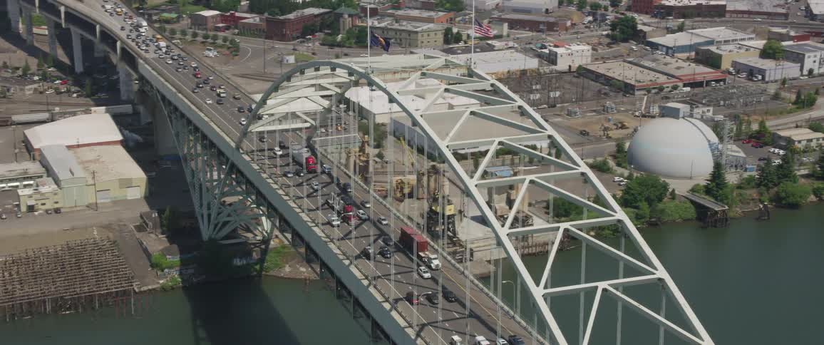 A bridge with heavy traffic over a body of water with a city in the background