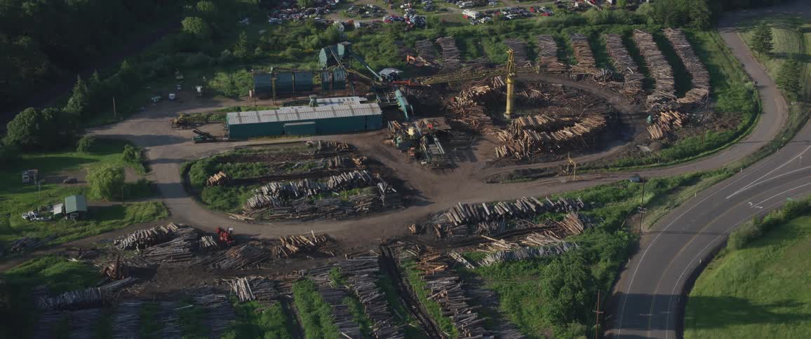 A construction crane sits in a compound surrounded by piles of wood
