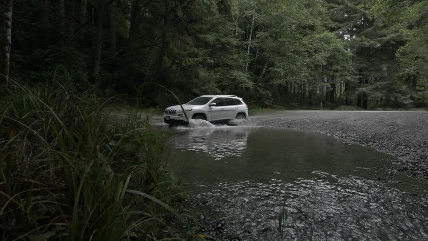 A car splashes through a deep puddle in the woods