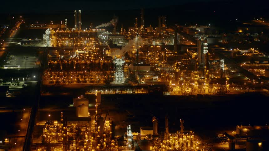 Sweepring aerial shot of a large refinery producing carbon emissions at night