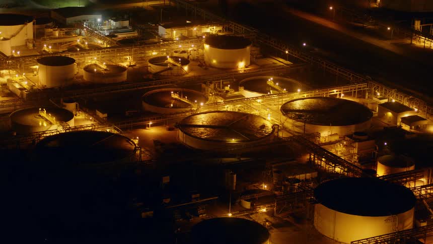 The camera flies over chemical pools in a large refinery