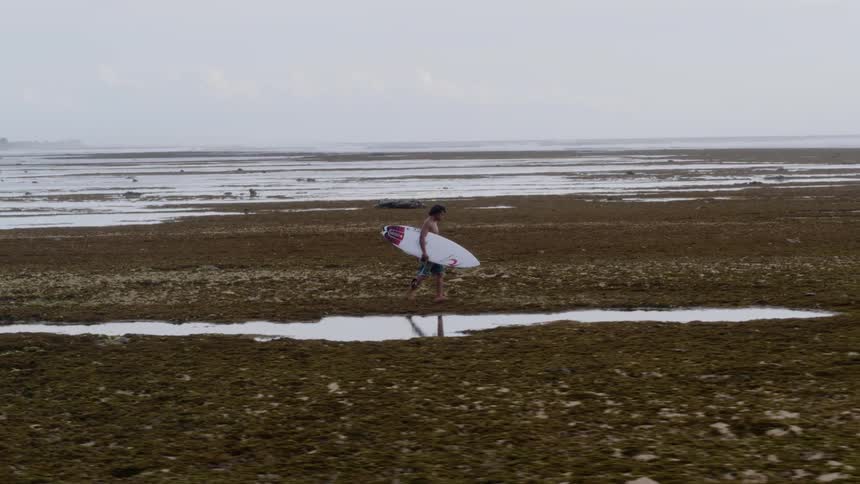 A man with a surfboard walks over a beach
