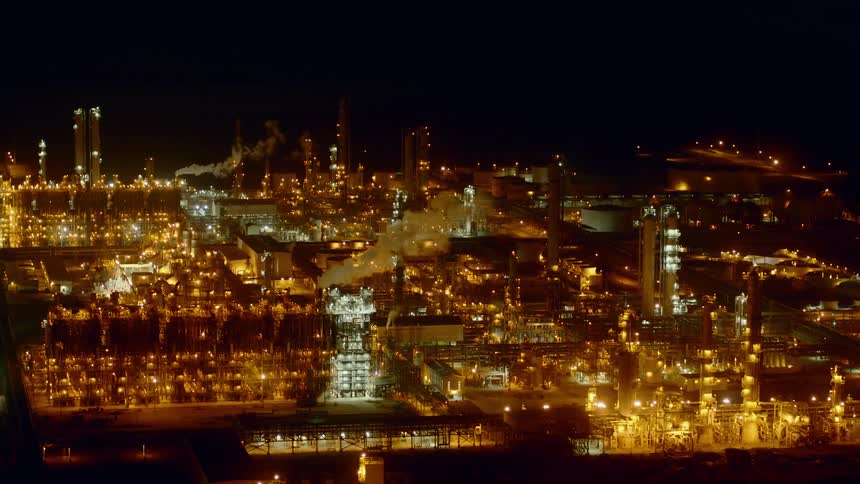 The camera flies over a refinery at night