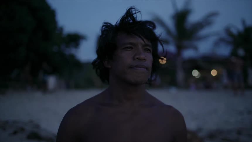 A man with messy hair stands on a beach at night and stares into the distance