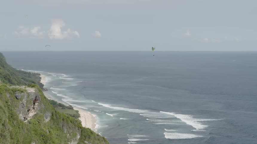 A cliff on the shore of a large body of water that people are parasailing towards