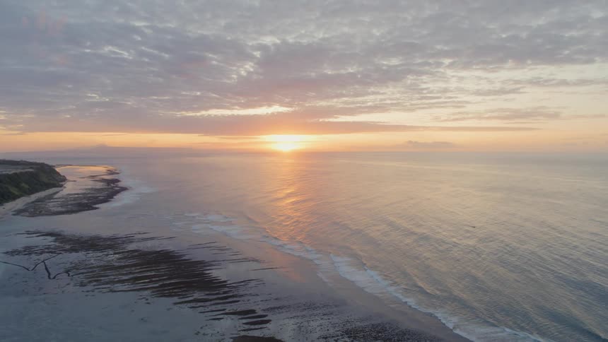 Ocean waves come to shore on a sandy beach at sunset