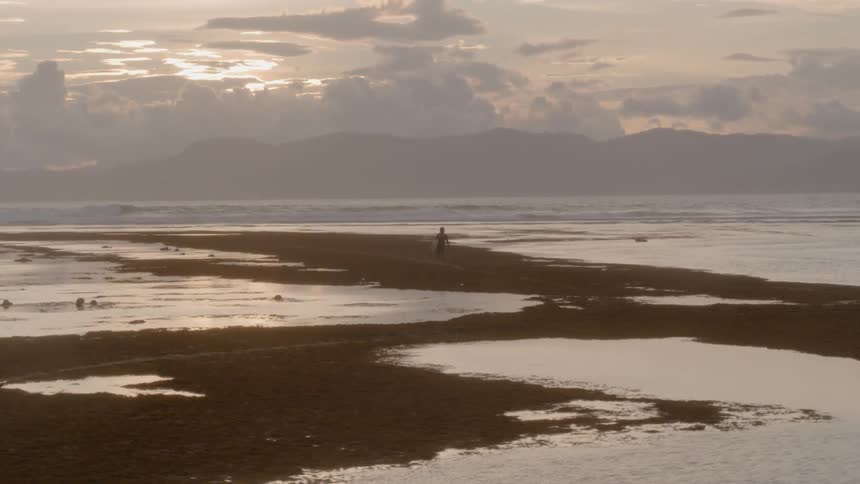 Man walks through tidal pools on beach under cloudy sky