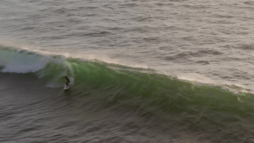 Man surfs wave on the surfing board at sunset