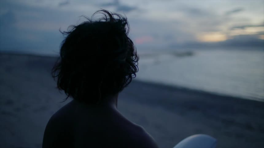 A person holds a surfboard and looks out at the ocean
