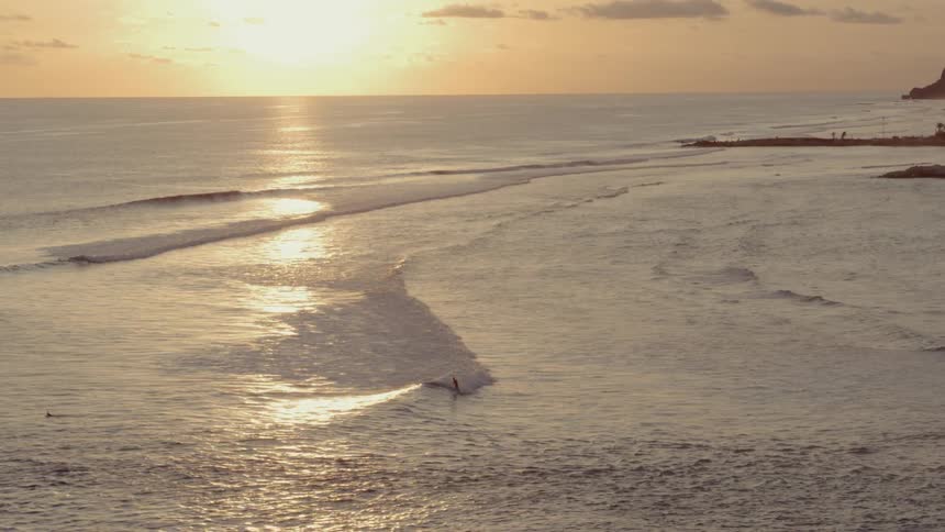 Man surfs among rolling waves and rip tide at sunset