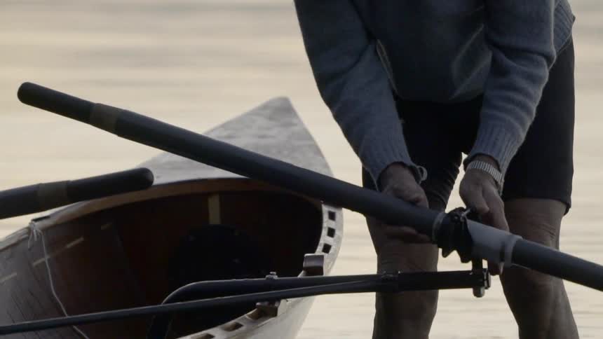 A man adjust and slides an oar through the oar lock while standing in the water near shore