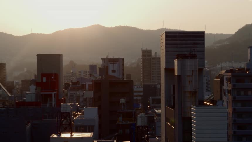 A city with lots of tall buildings sits in front of mountains under a sunset