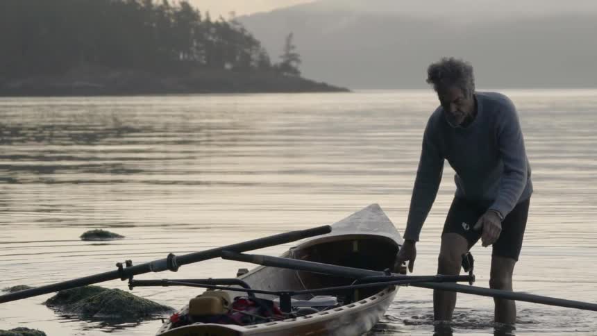 A man pulls on a kayak to bring it back to shore at dusk