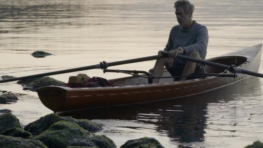 A man sits in a canoe holding onto the oar very close to the rocky shore