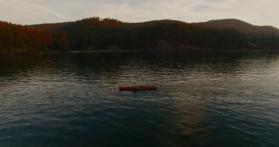A person rides a kayak on a river by a mountainous forest